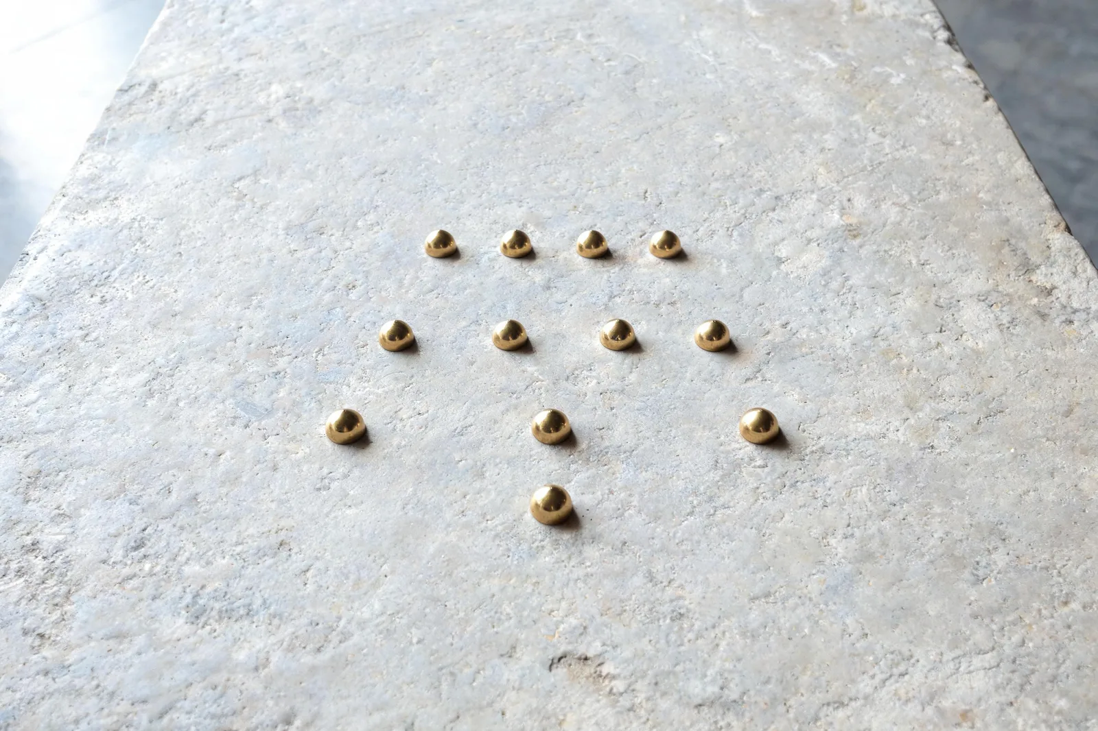 Ten small brass points laid out in four rising rows on a plain worn limestone slab, the fourth triangular figure, soft overcast light, the tarot 22 trumps number made visible