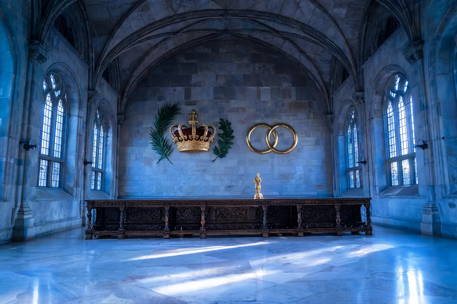 A 15th-century Milanese ducal hall at blue hour with a carved wooden table and a ducal crown on the wall